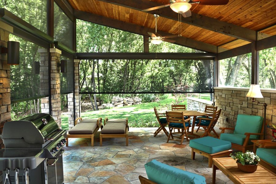 An outdoor patio with sitting areas, a grill, fans, and Insolroll outdoor motorized shades partially lowered.