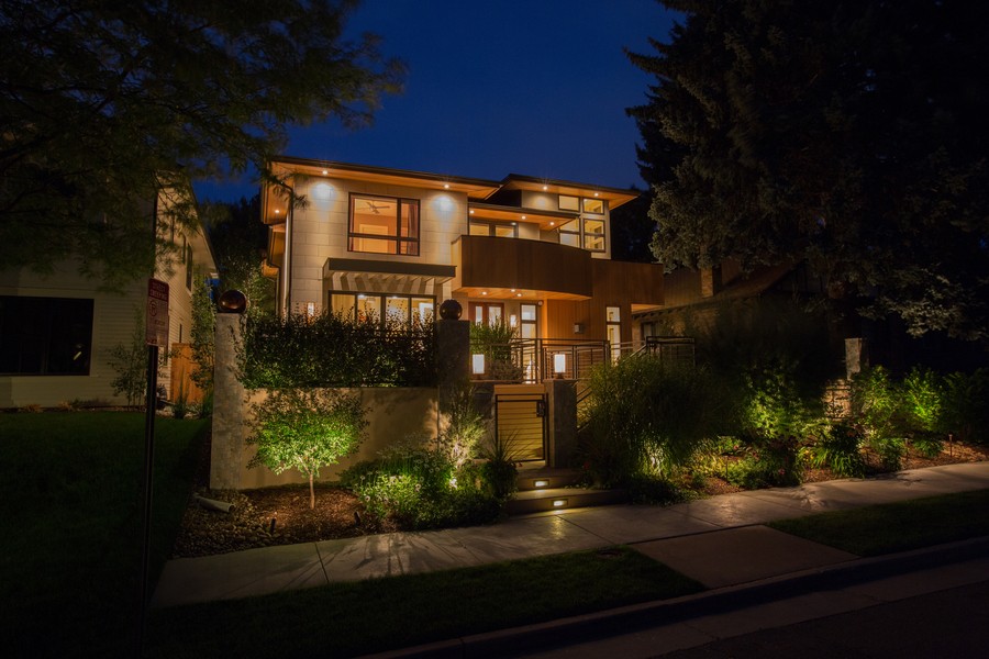 A multi-story house with a front gate illuminated by professional landscape lighting. 